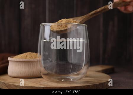 Fibra alimentare. Donna che aggiunge polvere di buccia di psico nell'acqua a tavola, primo piano Foto Stock