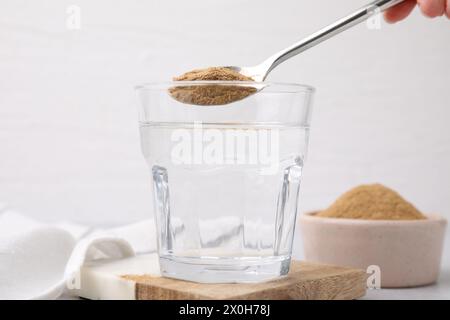 Fibra alimentare. Donna che aggiunge polvere di buccia di psico nell'acqua a tavola, primo piano Foto Stock