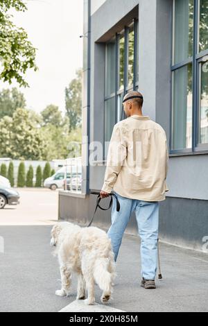 Un uomo afroamericano disabile con sindrome da miastenia gravis sta camminando un cane Labrador bianco lungo una strada in una dimostrazione di diversità e inclusione. Foto Stock