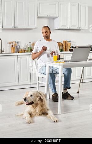 Un uomo afroamericano disabile collabora con il suo leale cane Labrador mentre lavora su un portatile a un tavolo. Foto Stock