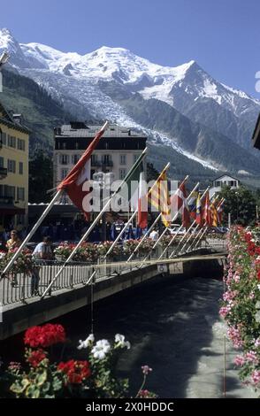 Bandiere colorate e scatole con gerani sono attaccate alla ringhiera di un ponte sull'Arve. Sullo sfondo, il massiccio del Monte bianco con il Monte bianco, l'Aiguille du GoÃ»ter e DÃme du Gouter e il Glacier des Bossons. [traduzione automatizzata] Foto Stock