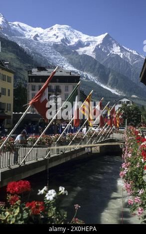 Bandiere colorate e scatole con gerani sono attaccate alla ringhiera di un ponte sull'Arve. Sullo sfondo, il massiccio del Monte bianco con il Monte bianco, l'Aiguille du GoÃ»ter e DÃme du Gouter e il Glacier des Bossons. [traduzione automatizzata] Foto Stock