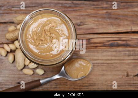 Gustosa pasta di arachidi in vaso e cucchiaio su un tavolo di legno, stendere in piano. Spazio per il testo Foto Stock