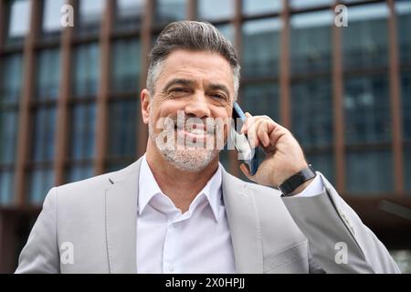 Uomo d'affari di mezza età, impegnato e felice, che fa una chiamata al telefono all'aperto. Foto Stock