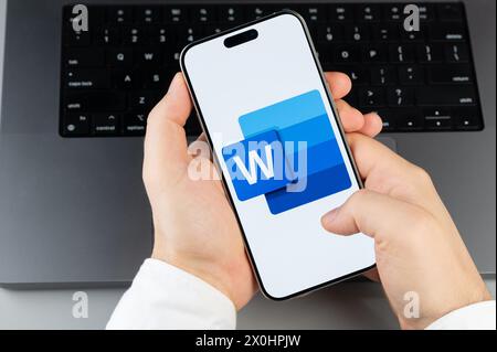 New York, Stati Uniti d'America - 6 aprile 2024: Popolare app mobile Word sullo schermo dello smartphone con le mani sullo sfondo della tastiera del laptop Foto Stock