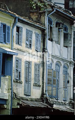 Vista lungo una fila di vecchi edifici di appartamenti a Singapore. Le facciate sono scolorite e vecchie. Gli otturatori sono parzialmente danneggiati. Dal tetto di una delle case cresce un piccolo albero. [traduzione automatica] Foto Stock