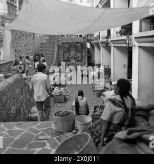 Vista su un cortile interno a Taxco. Ci sono molti giovani nel cortile. Alcuni sono seduti su scale di pietra. Ci sono molte scatole di legno intorno. All'altra estremità del cortile c'è un piccolo santuario. Sopra il cortile ci sono dei panni che si allungano tra gli edifici. [traduzione automatica] Foto Stock