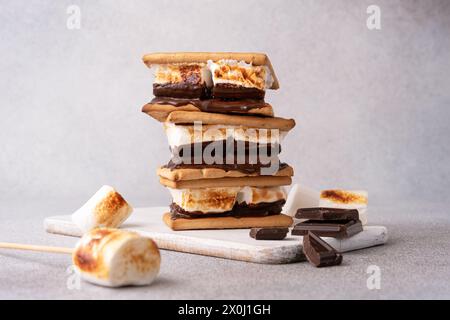 morse appena tostate con grandi marshmallow bianchi. Delizioso panino con marshmallow con cracker e cioccolato sul tavolo grigio, primo piano. Foto Stock