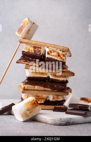 morse appena tostate con grandi marshmallow bianchi. Delizioso panino con marshmallow con cracker e cioccolato sul tavolo grigio, primo piano. Foto Stock