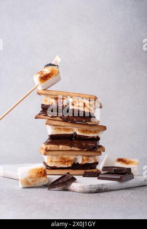 morse appena tostate con grandi marshmallow bianchi. Delizioso panino con marshmallow con cracker e cioccolato sul tavolo grigio, primo piano. Foto Stock