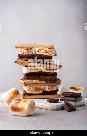 morse appena tostate con grandi marshmallow bianchi. Delizioso panino con marshmallow con cracker e cioccolato sul tavolo grigio, primo piano. Foto Stock