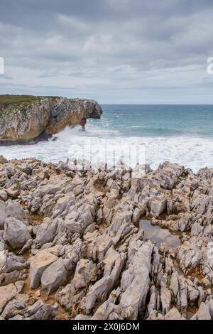 Una vista di una spiaggia rocciosa con scogli taglienti che si prosciugano fuori dall'acqua a Los Bufones de Llanes, Asturie. Le onde si infrangono contro la costa frastagliata, cr Foto Stock