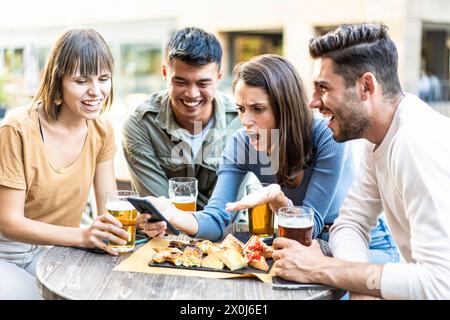 Momenti spontanei di amicizia rivelati. Un gruppo eterogeneo di amici condivide risate e sorprese con bevande e spuntini, incarnando lo spirito della m Foto Stock