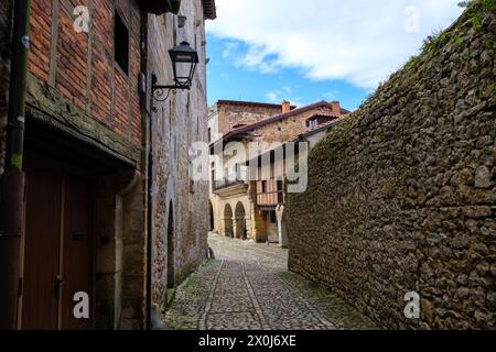 Una stretta strada acciottolata che si snoda attraverso una città vecchia a Santillana del Mar, Cantabria. L'architettura storica degli edifici in pietra e delle porte in legno Foto Stock