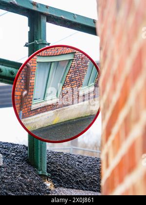 Uno specchio rotondo è appeso sul lato di un edificio in mattoni a Gothenburg, Svezia. Lo specchio riflette il paesaggio urbano circostante, aggiungendo un tocco Foto Stock