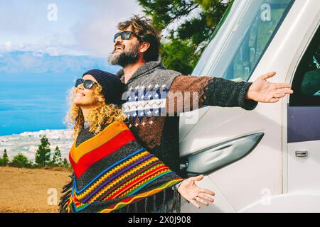 Concetto di vita del furgone e di destinazione di viaggio. Uomo e donna entusiasti per il nuovo arrivo nella natura aprendo le braccia contro il loro nuovo camper moderno casa. Campeggio gratuito con camper. Persone che vivono fuori dalla griglia Foto Stock