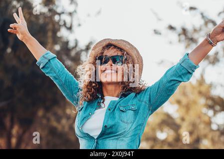 Gente overjoyed donna felice alzando le braccia con il gesto di vittoria e sorridendo con gli alberi verdi natura all'aperto sfondo. Allegre donne in attività turistiche fuori. Signora che si diverte Foto Stock