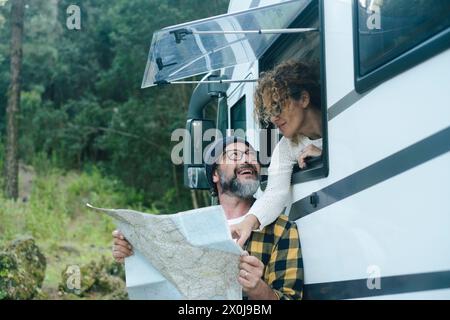 Una coppia di adulti utilizza la guida cartacea per scegliere la prossima destinazione di viaggio, godendosi la libertà e la vacanza all'esterno di un moderno camper. Persone nomadi. Uomo e donna viaggiatore a tempo pieno nel parco naturale Foto Stock