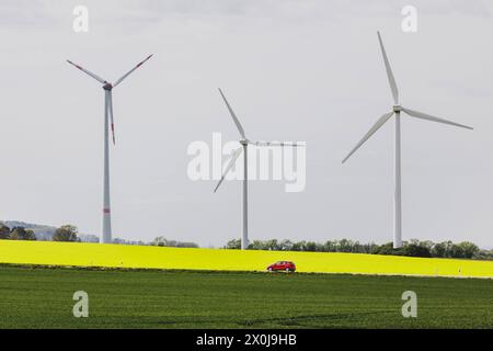 Ein Auto auf einer Landstrasse zeichnet sich ab vor einem Rapsfeld und Windraedern in Vierkirchen, 12.04.2024. Vierkirchen Deutschland *** Una macchina su una Foto Stock