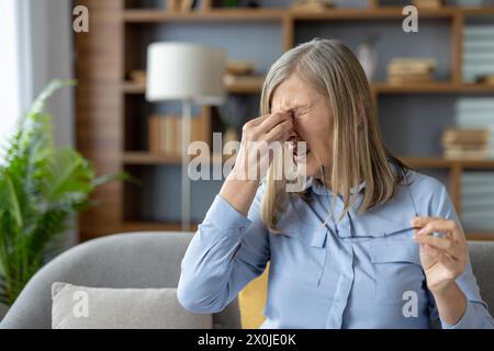 Donna matura a casa che tocca i suoi templi, si sente sopraffatta e stressata. Sembra angosciata e bisognosa di conforto. Foto Stock