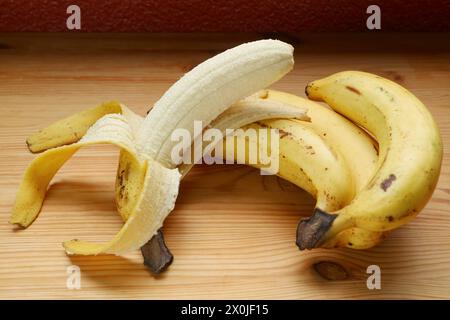 Banana sbucciata su un mazzo di non sbucciati isolati su un tavolo di legno Foto Stock