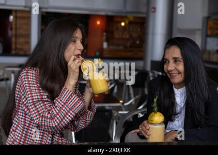 La mamma e la figlia latinoamericana chiacchierano, festeggiano e condividono un drink di frutta insieme. Festa della mamma e concetti di vita sana Foto Stock