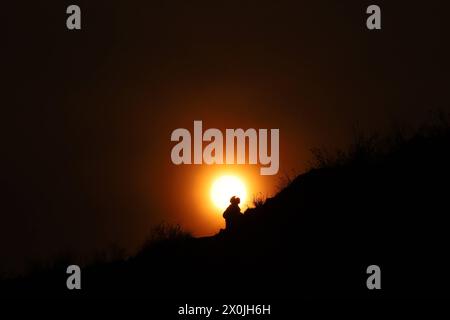 Ultimo tramonto dell'anno nepalese 2080 BS Una persona sale su un terreno mentre il sole tramonta contro le colline che circondano la valle di Kathmandu, mentre diventa l'ultimo tramonto dell'anno nepalese 2080 BS Bikram Sambat secondo il calendario georgiano nella periferia di Kathmandu il 12 aprile 2024. Nepal il 13 aprile 2024 festeggia il nuovo anno 2081 BS con grandeur e fervore. Copyright: XSubashxShresthax Foto Stock