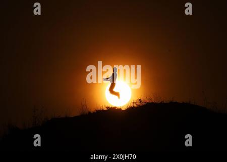 Ultimo tramonto dell'anno nepalese 2080 BS Un uomo salta mentre posa per una foto in piedi contro l'ultimo tramonto dell'anno nepalese 2080 BS Bikram Sambat secondo il calendario georgiano nella periferia di Kathmandu il 12 aprile 2024. Nepal il 13 aprile 2024 festeggia il nuovo anno 2081 BS con grandeur e fervore. Copyright: XSubashxShresthax Foto Stock