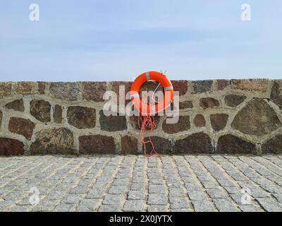 Un salvagente con 4 strisce riflettenti è fissato a un muro di pietra, in primo piano ci sono lastricati, Mar Baltico, Germania Foto Stock