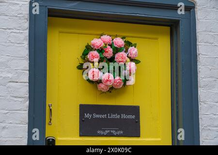 Porta d'ingresso gialla con una targa intitolata "My Sweet Little home" e una corona rosa di colore rosa Foto Stock