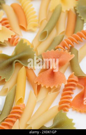 Macaroni tricolori di diversi tipi. Si trova su una superficie bianca. Primo piano. Foto Stock