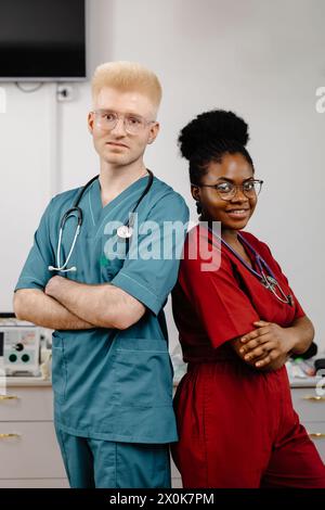 Due medici professionisti, che indossano cappotti bianchi, in piedi fianco a fianco in un ambiente ospedaliero. Sembrano concentrati e impegnati in conversazioni o console Foto Stock