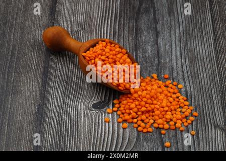 Lenticchie rosse in paletta di legno, isolate su fondo di legno. Foto Stock