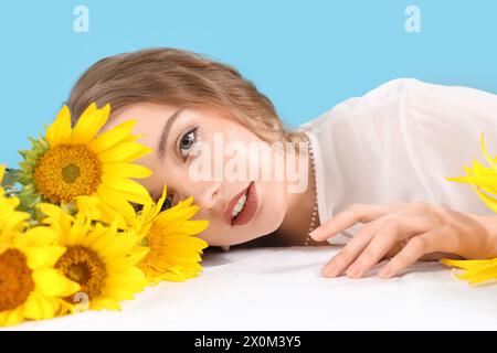 Giovane donna con bellissimi girasoli sul tavolo su sfondo blu, primo piano Foto Stock