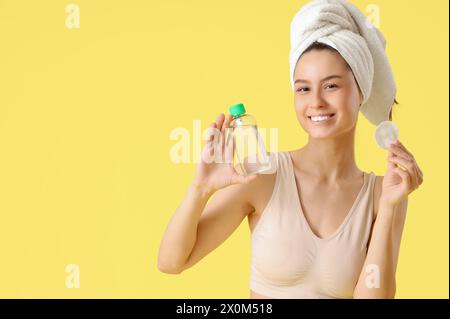 Giovane donna con batuffolo di cotone e acqua micellare su sfondo giallo Foto Stock