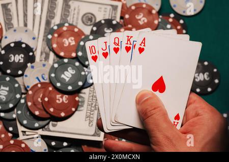 Royal Flush in poker nelle mani del giocatore sullo sfondo di chip di gioco e soldi nel primo piano del casinò Foto Stock