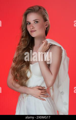 Ritratto di una donna bionda vestita con un corsetto a forma di scultura e una giacca gettata sulla spalla. Modello alla moda e sereno con lunghi capelli ondulati Foto Stock