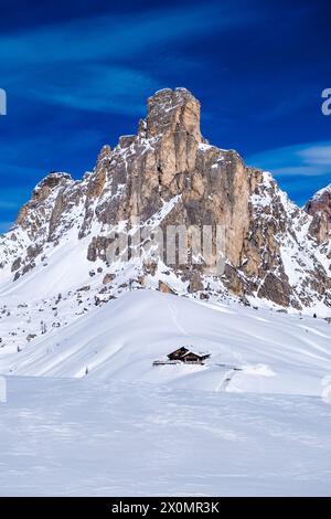 Pendii innevati del paesaggio alpino dolomitico intorno al passo di Giau in inverno, la cima di Ra Gusela e un rifugio in lontananza. Foto Stock