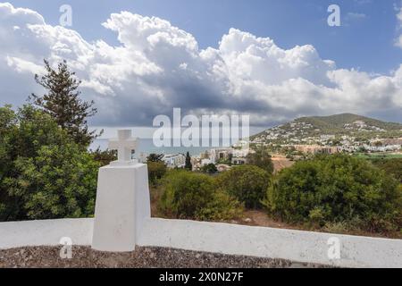 Vista dalla chiesa di Puig de Missa, caratterizzata da una croce bianca simbolica con lo sfondo panoramico della città di Santa Eulalia, i suoi paesaggi verdeggianti e la Foto Stock