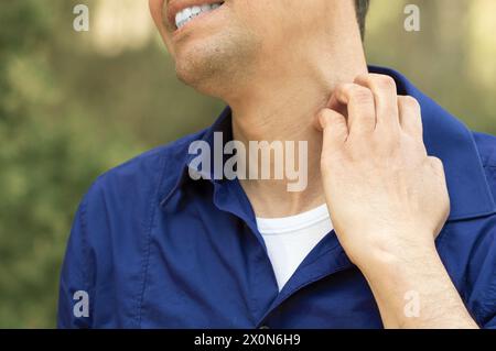 Primo piano di un uomo che soffre di prurito graffiare il collo in piedi all'aperto in un parco Foto Stock