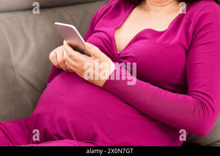 Primo piano di una donna incinta che SMS sul suo cellulare a casa Foto Stock