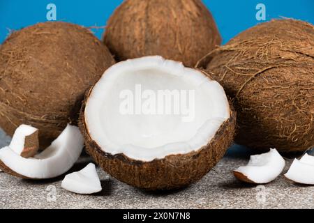 Noci di cocco intere e mezza noce di cocco su sfondo blu e grigio primo piano Foto Stock