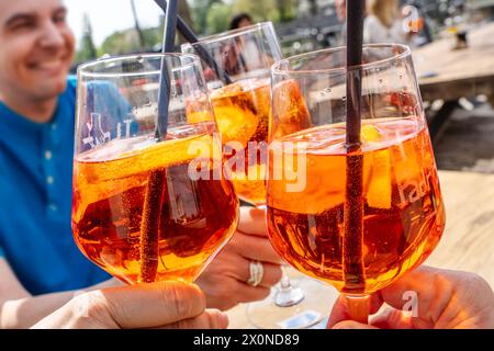 Aperol Spritz, Gäste stoßen mit Gläsern an, Frühling, Landshut, aprile 2024 Deutschland, Landshut, aprile 2024, drei Gläser Aperol Spritz, Leute stoßen mit den Getränken an, Papierstrohhalme, Alkohol, gastronomia, eiskalte Getränke, Erfrischung bei Frühlingstemperaturen um die 24 Grad, Wärme, Warm, draußen, Frühling, *** Aperol Spritz, ospiti brindisi con bicchieri, primavera, Landshut, aprile 2024 Germania, Landshut, 2024 aprile, tre bicchieri di Aperol Spritz, brindisi con le bevande, cannucce di carta, alcol, gastronomia, bevande ghiacciate, rinfresco in primavera con temperature intorno ai 24 gradi, calore, w Foto Stock