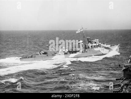 HMS FORMIDABLE 'SUL LAVORO'. OTTOBRE 1943, A BORDO FORMIDABLE, IN MARE CON ALTRE NAVI DELLA ROYAL NAVY. I SUOI AEREI SONO GLI "OCCHI" DELLA FLOTTA, A GUARDARE GLI U-BOOT E PRONTI A RESPINGERE UN TENTATIVO DI ATTACCO AEREO. - HMS FARNDALE, una delle escort che fuma vicino alla HMS FORMIDABLE Foto Stock