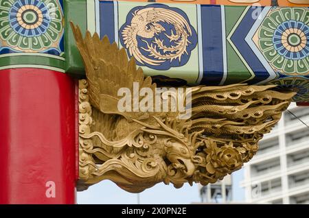 Un uccello rosso e oro è scolpito in una struttura in legno rossa e blu. L'uccello è un simbolo di buona fortuna e prosperità Foto Stock