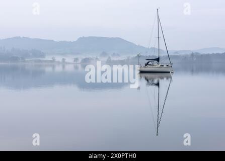 Splendida immagine di paesaggio tranquillo della mattina nebbiosa di primavera su Windermere nel Lake District con barche ormeggiate sul lago e lontane cime nebbiose Foto Stock