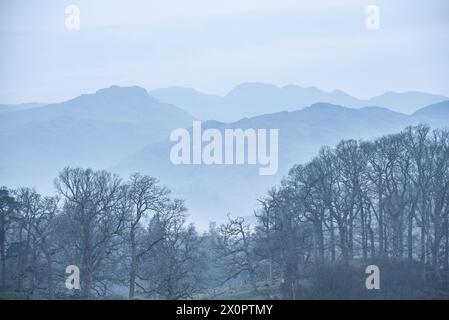 Splendida immagine di paesaggio tranquillo della mattina nebbiosa di primavera su Windermere nel Lake District con barche ormeggiate sul lago e lontane cime nebbiose Foto Stock