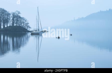Splendida immagine di paesaggio tranquillo della mattina nebbiosa di primavera su Windermere nel Lake District con barche ormeggiate sul lago e lontane cime nebbiose Foto Stock