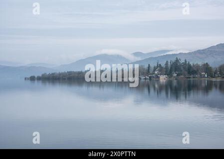 Splendida immagine di paesaggio tranquillo della mattina nebbiosa di primavera su Windermere nel Lake District con barche ormeggiate sul lago e lontane cime nebbiose Foto Stock