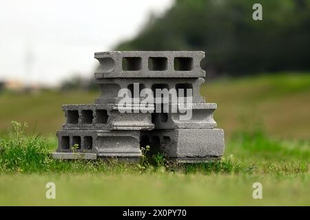 Un mucchio di blocchi cavi di calcestruzzo impilati uno sopra l'altro nell'erba. Foto Stock